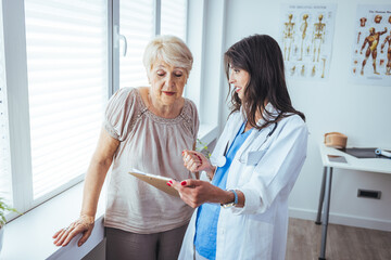 An senior woman speaks with her doctor during a routine check-up in the doctors office. Senior patient listens carefully to the mid adult female doctor. 