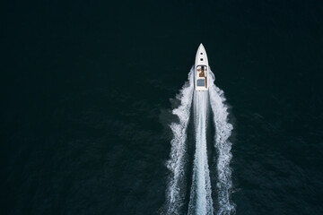White boat in motion top view. Large high speed open motor boat movement on dark water aerial view. Mega boat moves fast on the water.