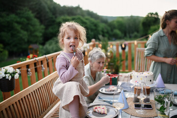 Little girl enjoying eating birthday cake during multi generation family celebration outside on patio.