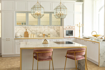 a close view of the white stylish kitchen with a cooking island in the luxurious interior of a modern apartment in light colors with stylish furniture.
