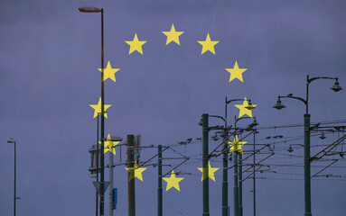 European Union flag with tram connecting on electric line with blue sky as background, electric railway train and power supply lines, cables connections and metal pole overhead catenary wire