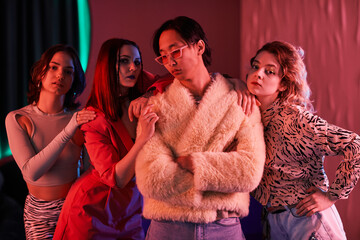 Group of young girls posing with extravagant Asian man in nightclub lit by pink neon light - obrazy, fototapety, plakaty