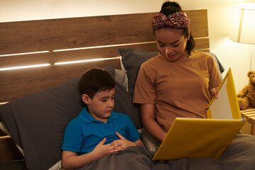 Mother reading book of fairytales to son before go to sleep