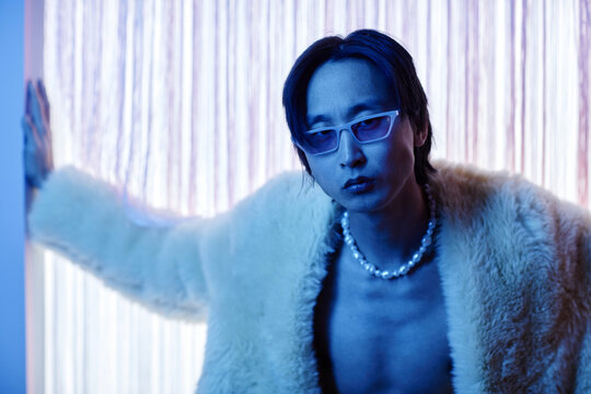 Portrait of handsome Asian man wearing party outfit and sunglasses looking at camera intensely in blue neon light