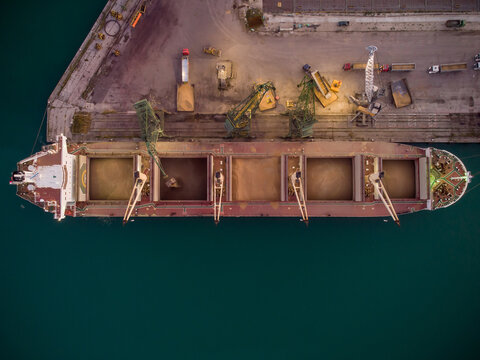 Aerial view of big cargo ship bulk carrier is loaded with grain of wheat in port at sunset