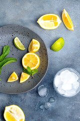 lemonade preparationю. glass with ice cubes. fresh ingredients lemon and mint on gray ceramic plate