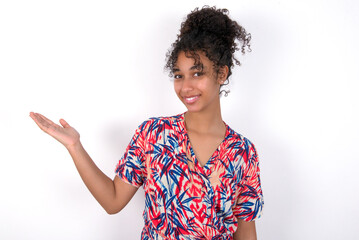 Positive glad Young African American woman wearing colourful dress over white says: wow how exciting it is, has amazed expression, shows something on blank space with open hand. Advertisement concept.