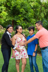 Family touching the belly of a pregnant woman while standing together in the backyard of their home.