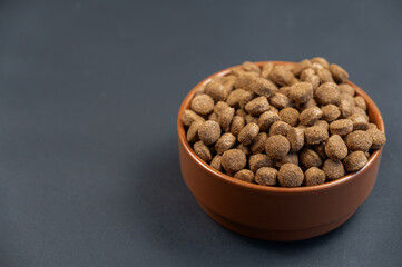 Bowl of dog food against a gray background. Round brown pellets in a ceramic bowl. Food for neutered and straitened pets. Healthy food. Angled view from above. Copy space for text and design elements