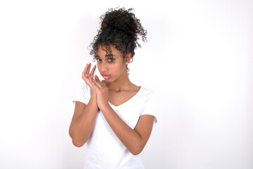 Surprised emotional Young beautiful girl with afro hairstyle wearing white t-shirt over white wall rubs palms and stares at camera with disbelief