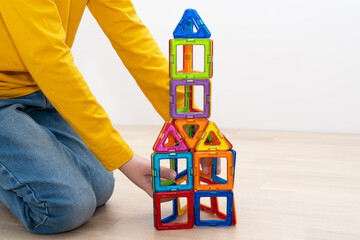 Boy assembling house from pieces of magnetic construction set.