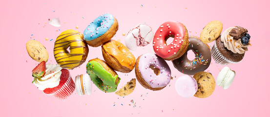 Donuts, cupcakes, cookies, macarons flying on pink background. Confectionery and sweets levitation...