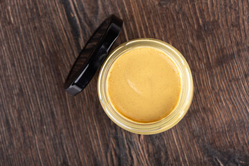 Top view of open glass jar with Dijon mustard and black lid on wooden background.