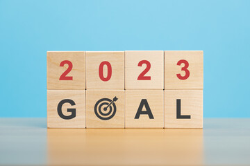 New year 2023. Stack of wooden blocks with number 2023, word goal and target icon on wooden table blue background. Business development strategy, advancement and goal concept.