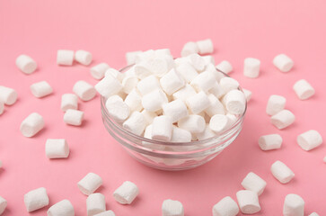 Fototapeta na wymiar Marshmallows on a pink background in a glass bowl. White marshmallow flat lay. Sweets and snacks for a snack. Chewing candies close-up. Copy space. Place for text. Winter food concept.