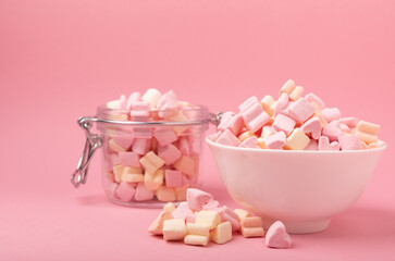 Marshmallow in a ceramic bowl and a glass jar on a pink background.Close-up strawberry flavored chewy candy.Snacks and snacks for parties.Spice for coffee and cocoa.Winter food concept.Place for text.