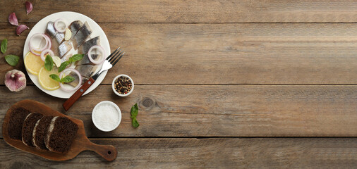 Sliced salted herring fillet served with basil, onion rings and lemon on wooden table, flat lay with space for text. Banner design