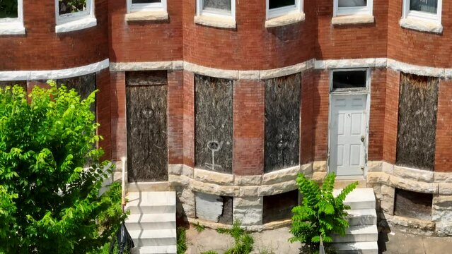 Abandoned boarded up rowhomes in USA. American poverty in inner city urban setting. Aerial tilt up reveal.