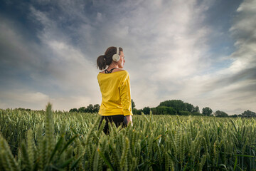 Woman wearing heaphones standing in a field, getting away from it all.