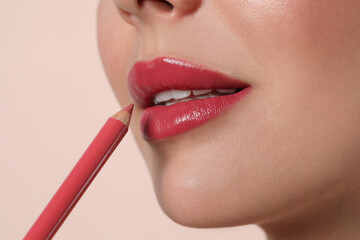 Naklejka premium Young woman applying beautiful pink lip pencil on light background, closeup