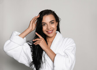 Beautiful young woman wearing bathrobe on light background