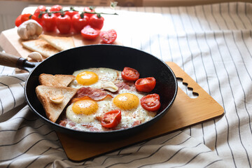 Delicious fried eggs with bacon and tomatoes in pan on table