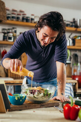 young man dressing salad in his home kitchen