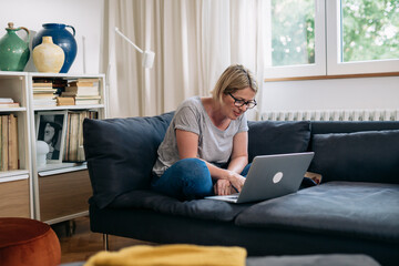 caucasian woman checking e mails on laptop sitting on sofa in living room