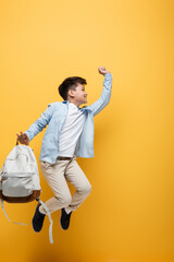Side view of asian schoolboy holding backpack and jumping isolated on yellow.