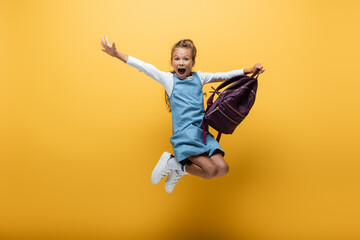 Fototapeta na wymiar Excited schoolkid with backpack jumping on yellow background.