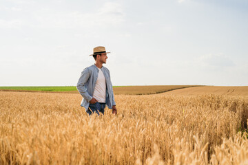Naklejka na ściany i meble Happy farmer is standing in his growing wheat field.