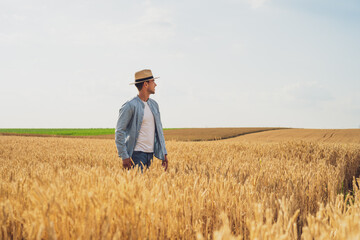 Happy farmer is standing in his growing wheat field.