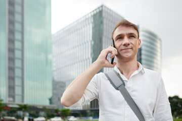 Portrait of smiling man with bag over shoulder talking on phone