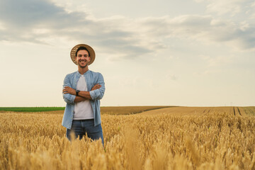 Happy farmer is standing in his growing wheat field.