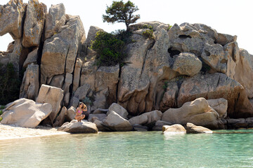 Fototapeta premium Beautiful mediterranean beach landscape with turquoise clear water and a young woman crouching on a rock