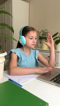 little girl wearing headphones, watching webinar, listening to online course, communicating via conference, video call, learning language on app, laughing, studying with teacher, lesson looking at lap