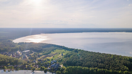 Aerial view of lake and small village on the peninsula. Sunset evening light by calm water on warm beautiful summer day.