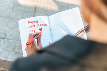 Woman writes in a notebook, holds felt-tip pen in her left hand.Outdoors summer evening park....