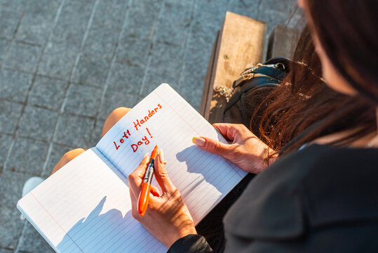 Young Woman lefty writes in a notebook. holds felt-tip pen in her left hand.Outdoors summer evening park. Left-handers Day August 13th.Closeup.