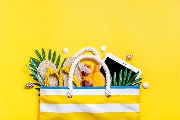 Swimming accessories - trendy beach bag with stripes, black glasses, white tablet, palm leaf, yellow flip flop on yellow background Flat lay Top view Summer, travel, vacation concept - 512349729
