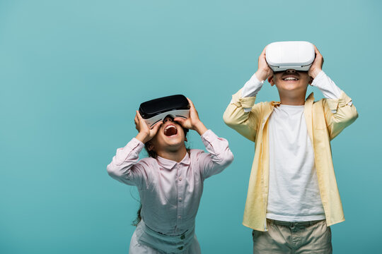 Excited preteen kids playing video game in vr headsets isolated on blue.