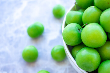 Green plums in a bowl on marble background.