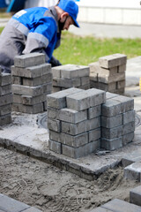 Bricklayer in work clothes sits on sidewalk and lays out paving slabs. Sight of working man in open air. Professional builder makes arrangement of territory summer day. Real scene.