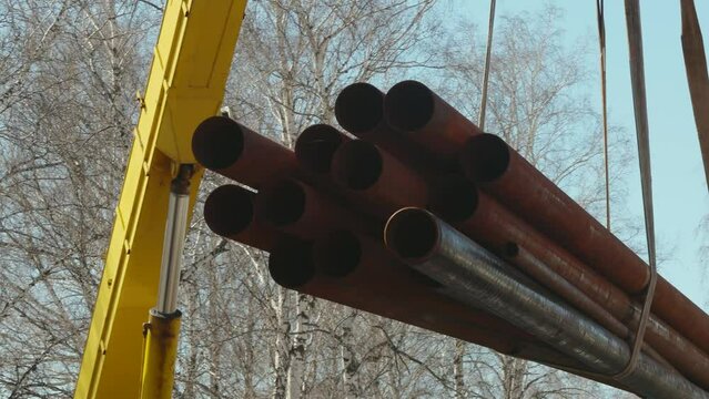 Video 4k. Slingers unload pipes with crane for construction on street. Real workflow scene