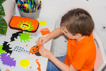 happy schoolboy with his crafts. a child at home creates bright decorations for the holiday. the working process. glues applications from colored paper