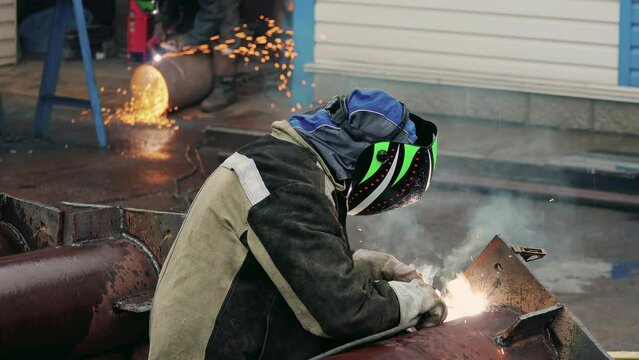 View of welder near pipe at work. Video 4k resolution. Welder in protective mask welds pipe and sparks fly. Industrial construction. Real workflow.