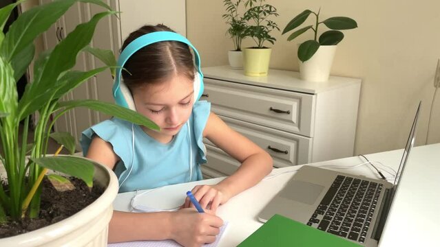 Happy little girl wear headphones, watch webinar, listen to online course, communicate via conference, video call, learn language on app, laugh, study with teacher, lesson look at laptop at home. High