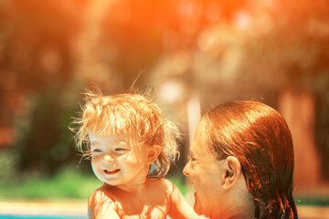 A woman teaches a baby to float on the water and swim. Happy child is having fun. Summer outdoor fun in the pool in the villa. Mom and daughter in the pool. Family happiness