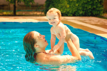 Mom and daughter in the pool. Happy child is having fun. The woman throws up and holds the baby up. Family happiness. Summer outdoor fun in the pool in the villa