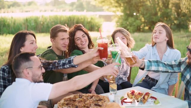 Group of friends are relaxing together outdoor. Young cheerful people clink glasses and laugh. Flare effect.